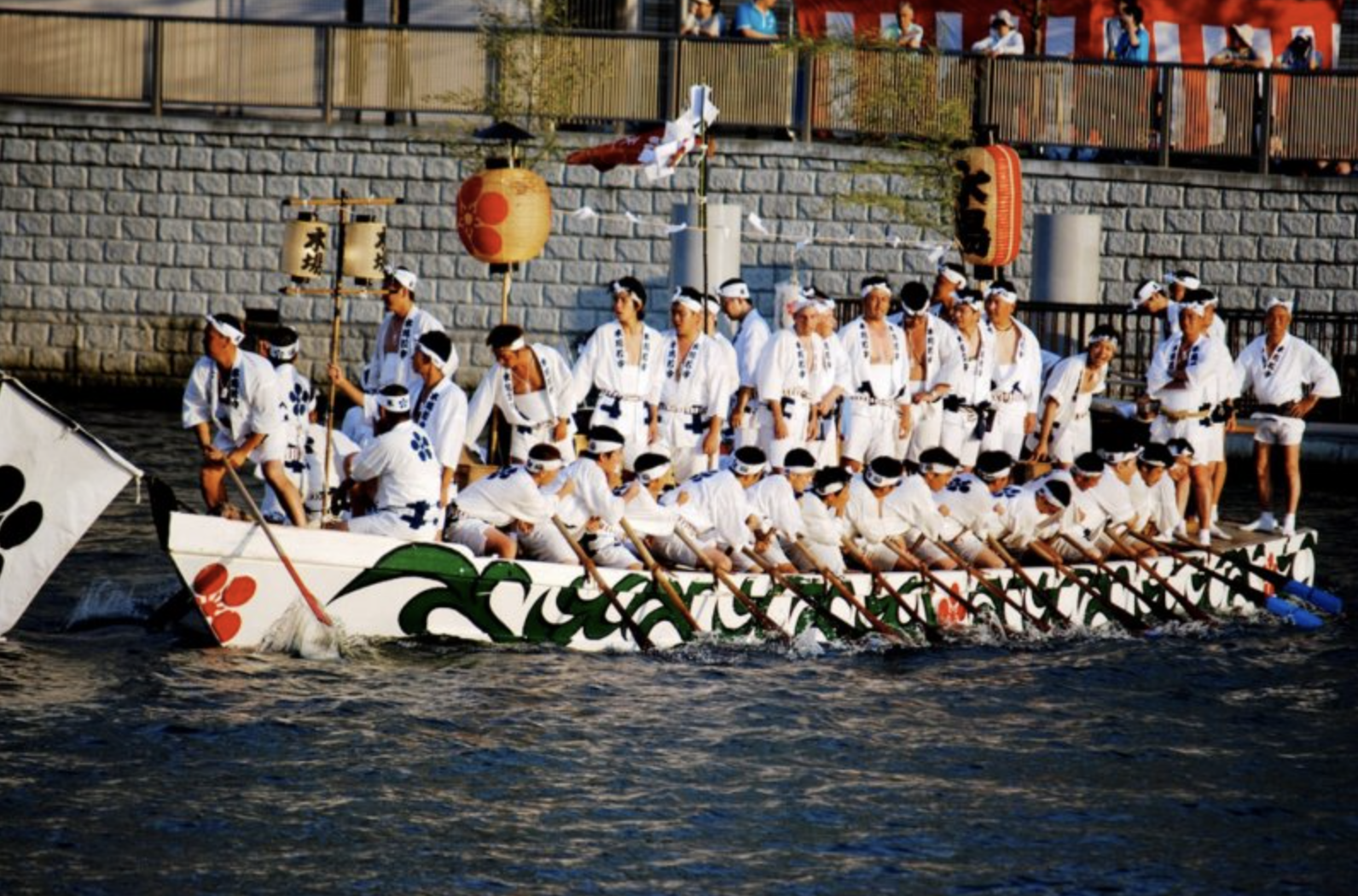 Men in white traditional attire rowing a large decorated boat during Tenjin matsuri festival