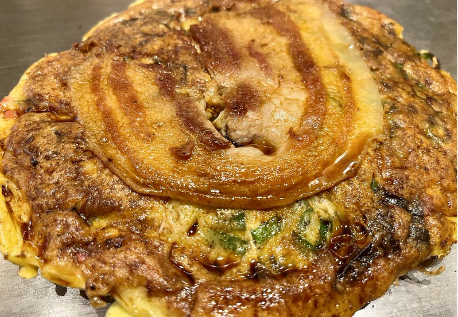 Savory Japanese negiyaki pancake topped with grilled pork belly