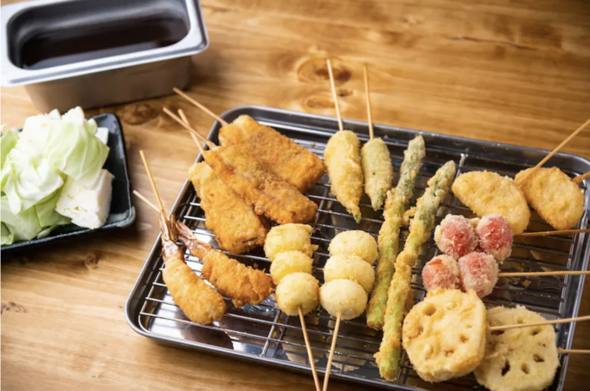 Assorted Japanese kushikatsu deep-fried skewers on a metal rack with cabbage and dipping sauce