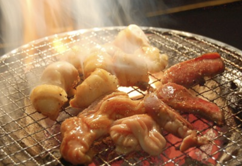 Assorted horumon offal grilling on a charcoal mesh with rising smoke