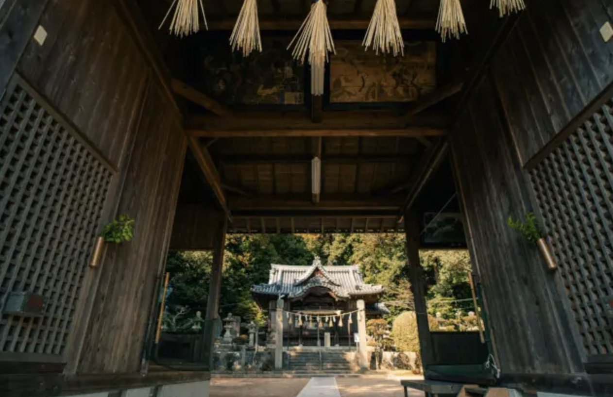 View of a traditional Shinto shrine building through a wooden gateway with sacred ropes
