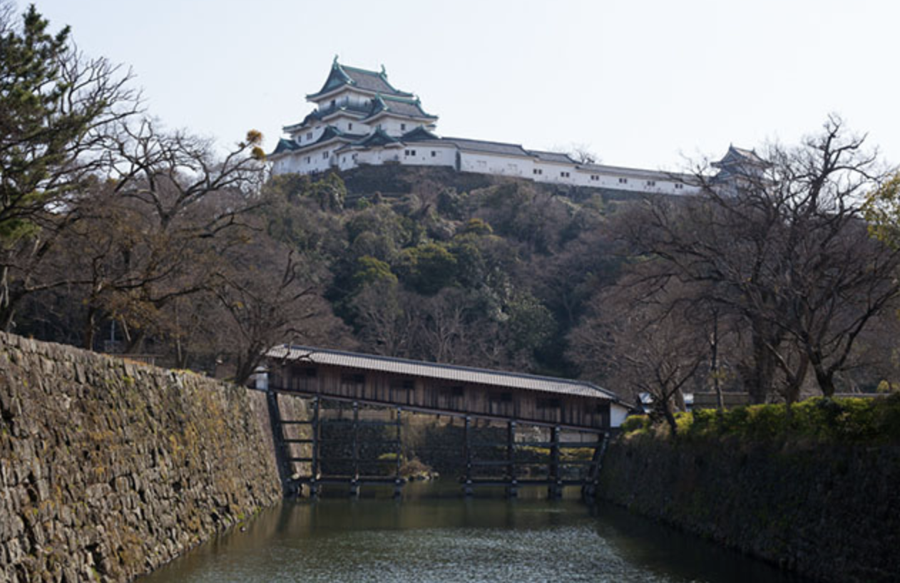 Wakayama Castle on a hill with a wooden bridge crossing the moat
